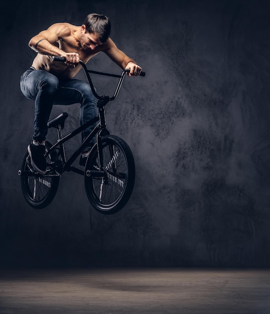 Gratis foto sterke shirtloze man, maakt een acrobatisch figuur met bmx in een studio. geïsoleerd op een donkere achtergrond.