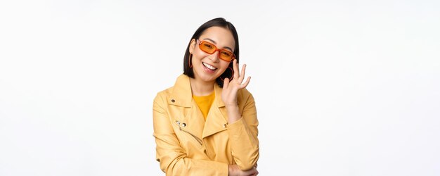 Stijlvol Aziatisch meisje met een zonnebril die lacht en er cool uitziet terwijl ze op een witte achtergrond staat