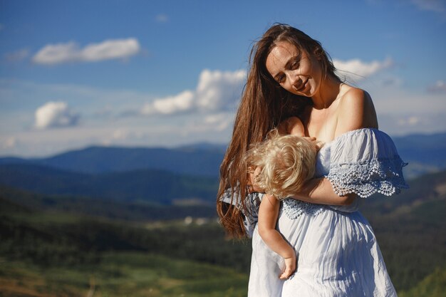Stijlvol gezin in de bergen. Moeder en dochter op een hemelachtergrond. Vrouw in een witte jurk.
