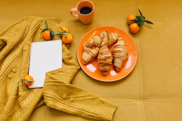 Stijlvol winterbeeld in oranje kleuren van bovenaf van gebreide trui, croissants, clementines en notitieboekje op tafel