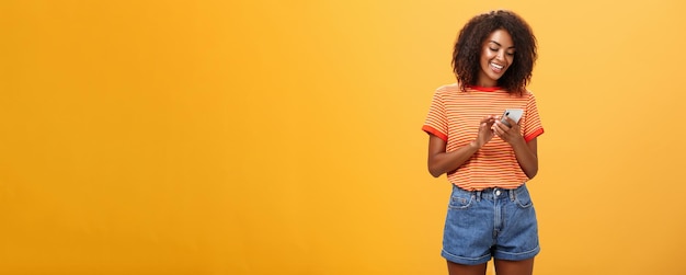 Stijlvol zorgeloos meisje sms'en vriend komt tevreden over oranje muur staan in stijlvolle denim sh