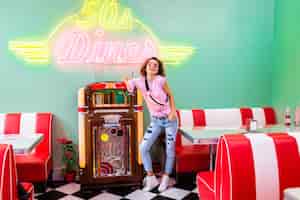 Gratis foto stijlvolle aantrekkelijke lachende vrouw in retro vintage 50's café bij muziek jukebox drinken milkshake cocktail in hipster outfit plezier lachen in vrolijke stemming