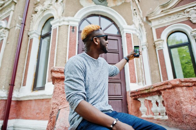 Stijlvolle Afro-Amerikaanse jongen op grijze trui en zwarte zonnebril poseerde op straat Modieuze zwarte man die selfie maakt op telefoon