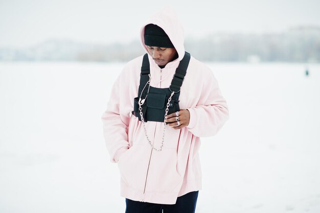 Stijlvolle Afro-Amerikaanse man in stedelijke stijl in roze hoodie poseerde in de winter aan het bevroren meer