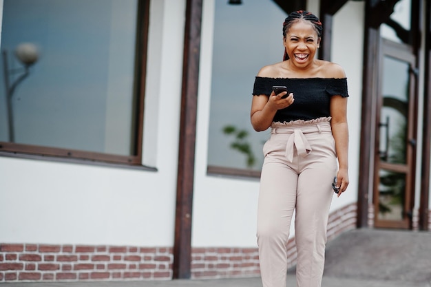 Stijlvolle Afro-Amerikaanse vrouw poseerde buiten en met behulp van mobiele telefoon