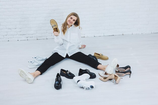 Stijlvolle blondine die schoenen kiest terwijl ze op de vloer zit zijaanzicht van veel damesschoenen op de vloer een keuze uit stijlvolle schoenen