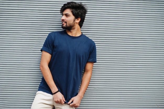 Stijlvolle casual Indiase man draagt blauwe t-shirt poseren tegen grijze muur