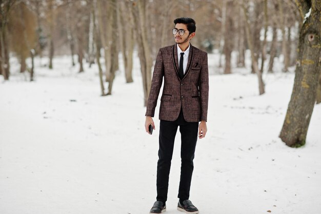 Stijlvolle Indiase student man in bruin pak en bril poseerde op winterdag buiten