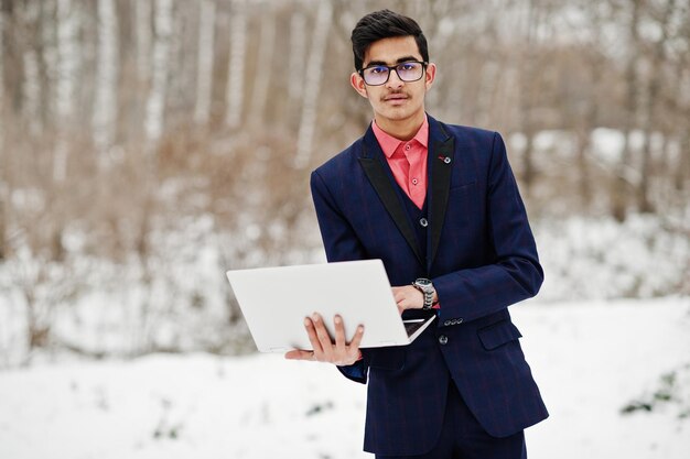 Stijlvolle Indiase student man in pak en bril poseerde op winterdag buiten met laptop bij de hand
