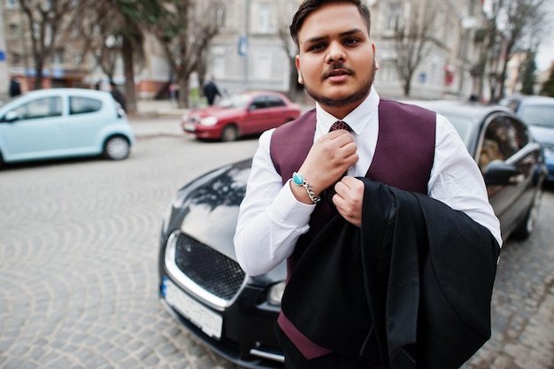 Stijlvolle Indiase zakenman in formele kleding bond zijn das vast en stond tegen zwarte zakenauto op straat van de stad
