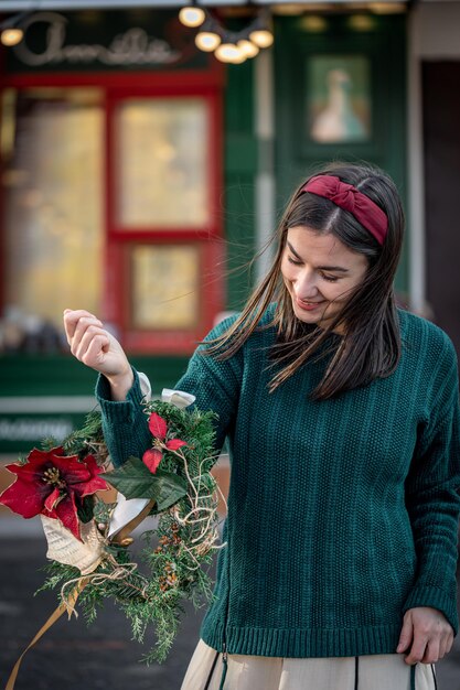 Stijlvolle jonge vrouw met een kerstkrans in rode en groene kleuren