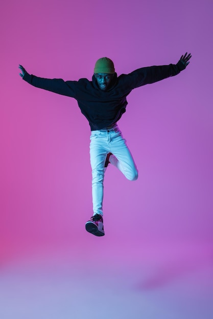 Gratis foto stijlvolle jongeman in moderne streetstyle outfit geïsoleerd op gradiënt achtergrond in neonlicht afro-amerikaanse modieuze model in look boek muzikant uitvoeren