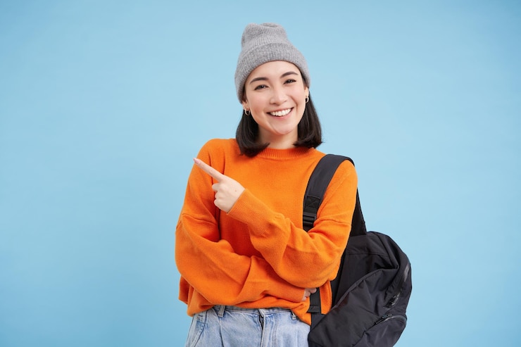 Gratis Foto stijlvolle koreaanse vrouw met hoed houdt de vinger van de rugzak vast op reclameshows promo-aanbieding banners