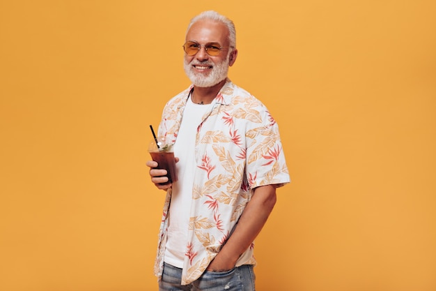 Stijlvolle man in bril houdt cocktail vast om op oranje muur te gaan
