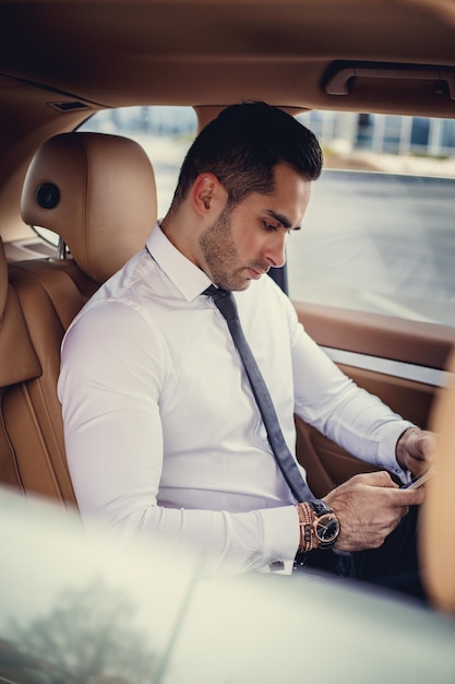 Stijlvolle man in een wit overhemd met smartphone in een luxe auto.