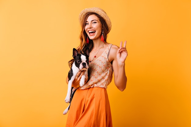 stijlvolle meisje Franse bulldog houden en lachen. Optimistische roodharige dame ontspannen in de studio met haar hond.