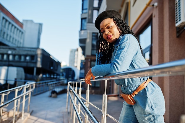 Stijlvolle modieuze Afro-Amerikaanse vrouwen in spijkerbroek en zwarte baret tegen modern gebouw