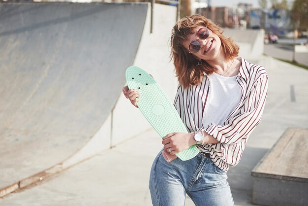 Stijlvolle mooie jonge vrouw met een skateboard, op een mooie zonnige zomerdag.