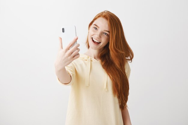 Stijlvolle roodharige meisje dat selfie met een tevreden glimlach neemt