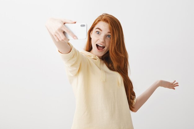 Stijlvolle roodharige vrouw die selfie neemt en iets laat zien
