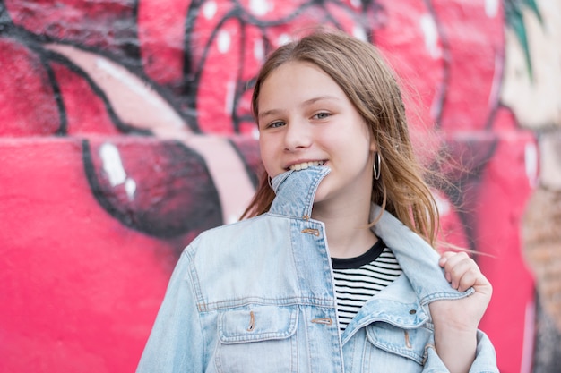 Stijlvolle tienermeisje met kraag van denim shirt in zijn mond tegen graffiti muur