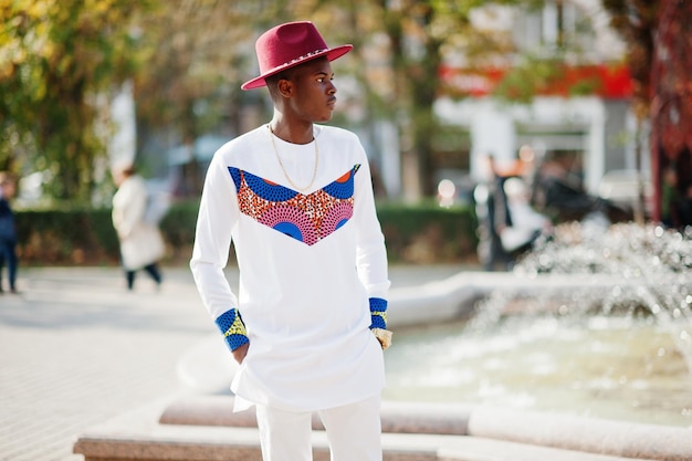 Stijlvolle trendy Afro-Frankrijk man in rode hoed en witte outfit geposeerd op herfstdag Black African Model Guy