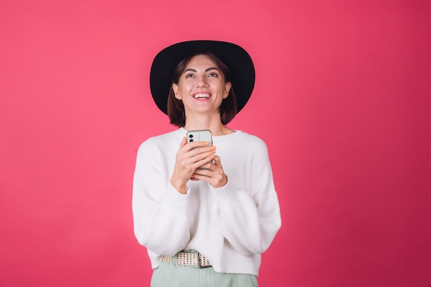 Stijlvolle vrouw in witte casual trui en hoed op rood roze muur