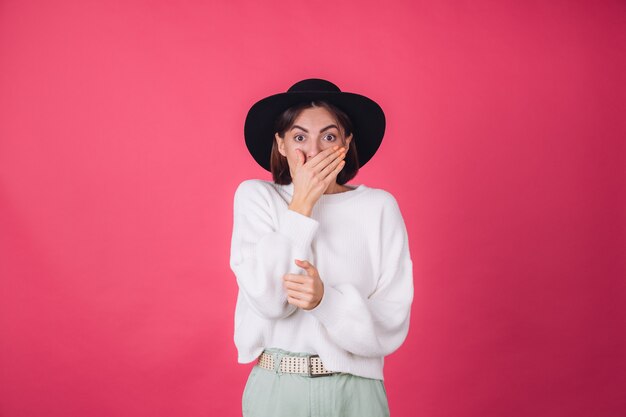 Stijlvolle vrouw in witte casual trui en hoed op rood roze muur