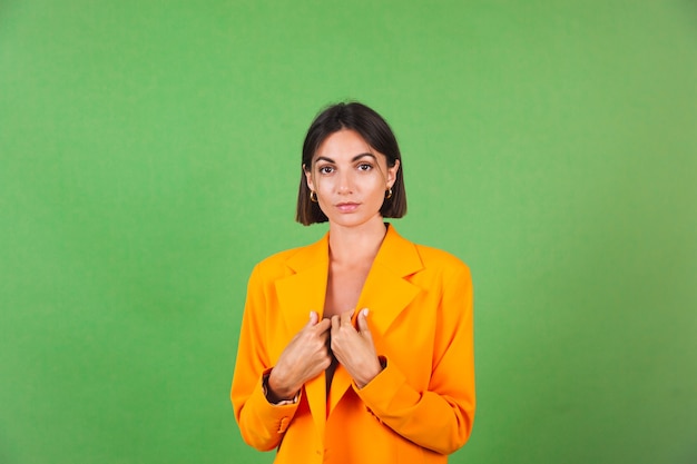 Stijlvolle vrouw in zijden beige jurk en oranje oversized blazer op groen, positieve emoties glimlach