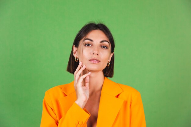 Stijlvolle vrouw in zijden beige jurk en oranje oversized blazer op groen, positieve emoties glimlach