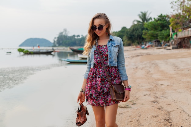 Stijlvolle vrouw in zomerkleding vakantie wandelen op het strand met schoenen in de hand