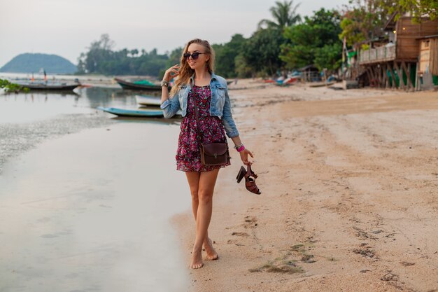 Stijlvolle vrouw in zomerkleding vakantie wandelen op het strand met schoenen in de hand