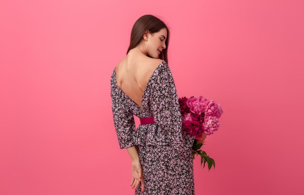 Stijlvolle vrouw op roze in trendy zomerjurk poseren met peony bloemen boeket, uitzicht vanaf achterkant