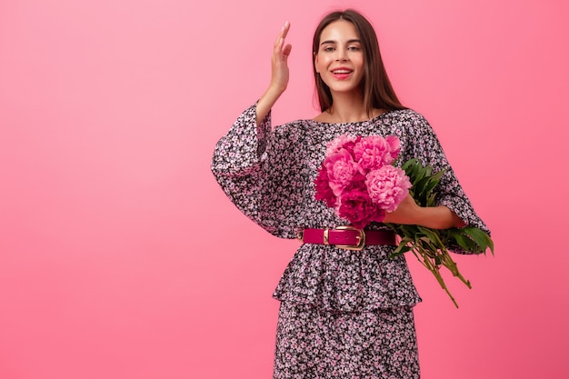 Stijlvolle vrouw op roze in trendy zomerjurk poseren met peony bloemen boeket