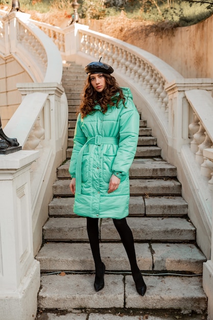 Stijlvolle vrouw poseren in winter herfst mode trend blauwe puffer jas en hoed baret in oude mooie straat trappen dragen hoge hak schoenen