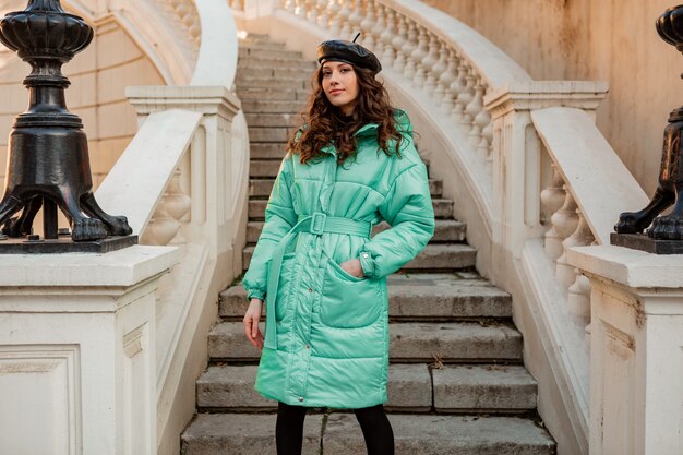 Stijlvolle vrouw poseren in winter herfst mode trend blauwe puffer jas en hoed baret in oude mooie straat trappen