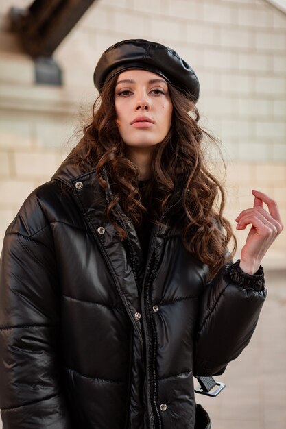 Stijlvolle vrouw poseren in winter herfst mode trend zwarte puffer jas en lederen hoed baret in oude mooie straat hoge hakken dragen