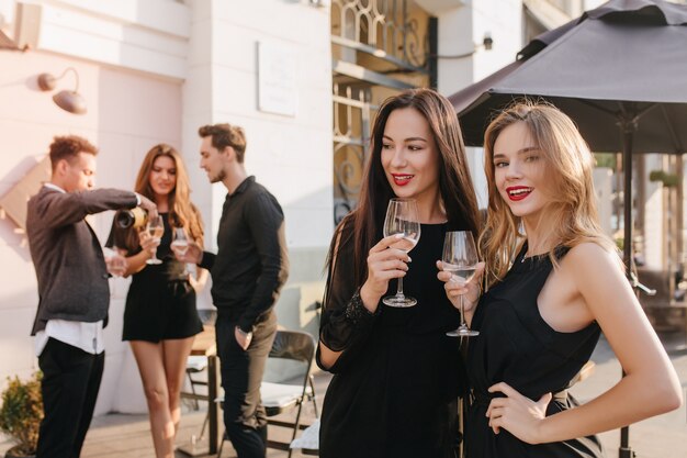 Stijlvolle vrouwen die iets bespreken terwijl ze champagne drinken op straat