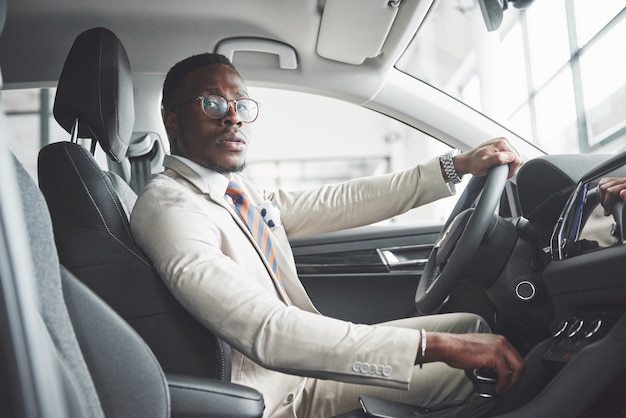 Stijlvolle zwarte zakenman achter het stuur van een nieuwe luxeauto. Rijke Afro-Amerikaanse man.