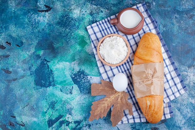 Stokbroodbrood, bloem, ei en melk op een theedoek, op de blauwe achtergrond.