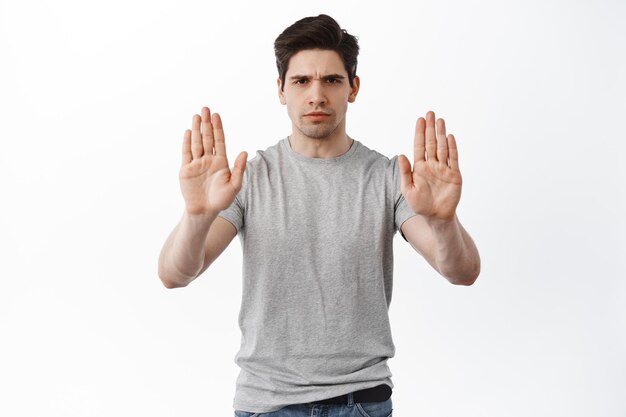 Stop ermee, houd afstand. Ernstige fronsende man die een gebaar van blokkering toont, handen uitstrekt om iets af te wijzen of te weigeren, actie te verbieden, staande op een witte achtergrond