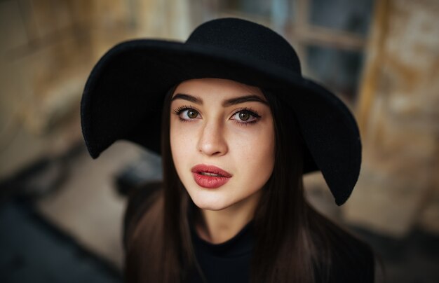 Straatportret van jonge casual dame in hoed, zwarte kleding, rode lippen