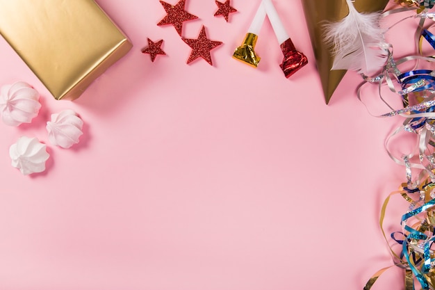 Streamers; ster stickers; geschenkdoos; feesthoed; veer; zephyrs en partijblazers op roze achtergrond