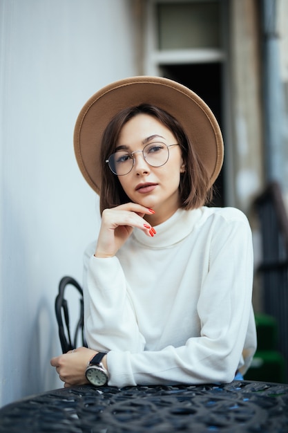 Street fashion mooie vrouw met rode manicure en transparante glazen zitten aan de tafel