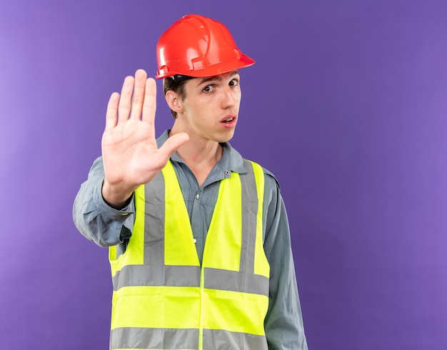 Strikt kijken naar camera jonge bouwer man in uniform met stopgebaar