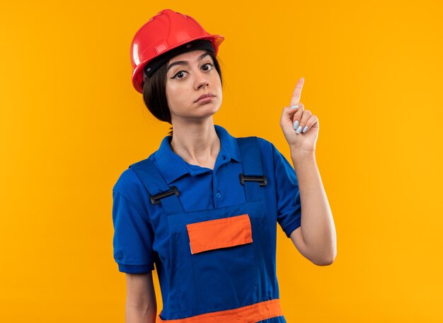 Strikt kijken naar camera jonge bouwer vrouw in uniforme punten naar boven