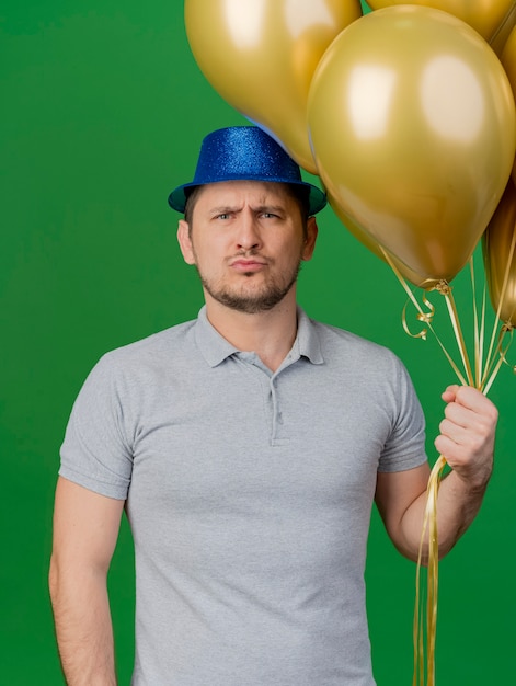 Gratis foto strikte jonge feest man met feestmuts met ballonnen geïsoleerd op groen