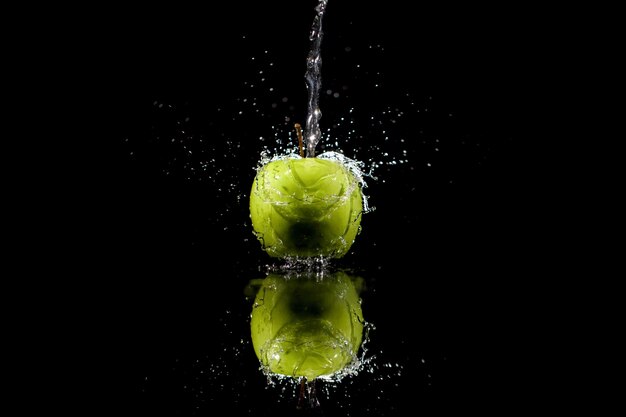 Strim van water giet op groene appel op zwarte achtergrond