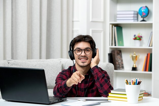 Student online jonge kerel in geruit overhemd met bril die op computer studeert en naar voren wijst