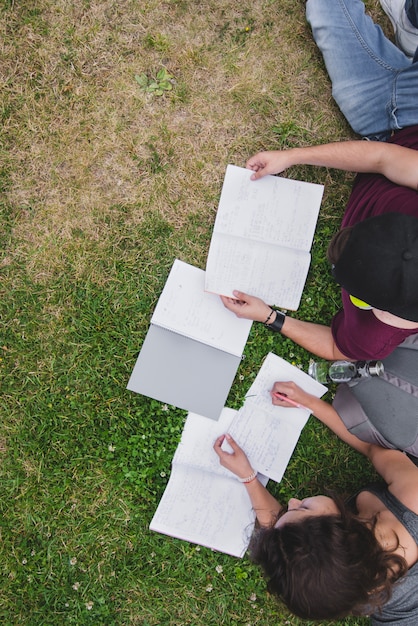 Studenten liggen op gras met notitieboekjes studeren